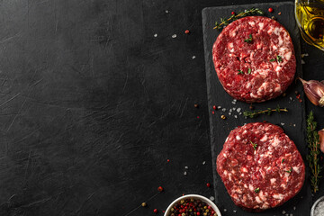 Raw beef hamburger patty or cutlet with herbs and spices for cooking on dark background. top view