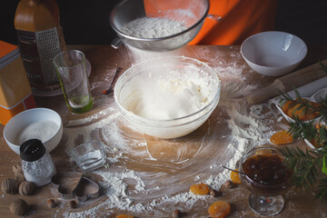 Fototapeta na wymiar A girl sifts flour over a bowl of dough. Preparation of cottage cheese cookies with dried apricots and nuts and apricot jam. The concept of home baking. Close-up, kitchen utensils, selective focus.