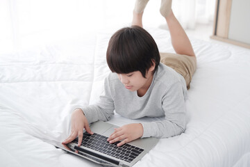 Fototapeta na wymiar Smiling Asian little boy is studying and doing homework with laptop in bedroom. Homeschool and quarantine during Covid-19 virus epidemic concept. Distance Learning Online Education