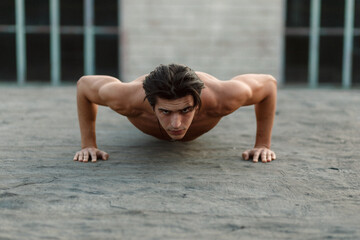 Fototapeta na wymiar Young muscle handsome man does push-ups with naked torso.
