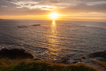 Orange sunset over the Atlantic Ocean seen from the rocky coastline of Barra Island, in the Outer...