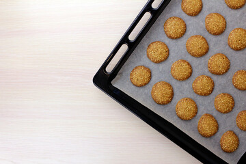 Cooked cookies on baking paper and on a black baking sheet on a wooden table