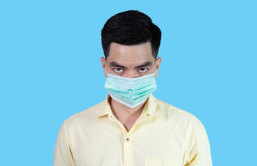 Close up COVID-19 Coronavirus portrait handsome young asian man wearing yellow shirt and sneezing mask protection from covid 19 isolated on blue background in studio. Asian man people. 