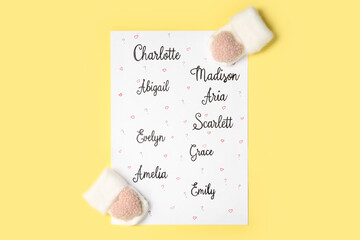 List of different baby names and newborn mittens on yellow background, flat lay