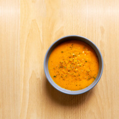 Creamy pumpkin soup  with chopped parsley and  thyme herb, cream and pumpkin with  pepper served in gray bowl on wooden table background. top view