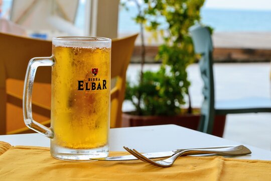 Elbar beer in a glass. Glass with Birra Elbar sign and logo with cold beer inside it. Beer on the table in the outdoor restaurant. Durres, Albania - June 5 2019
