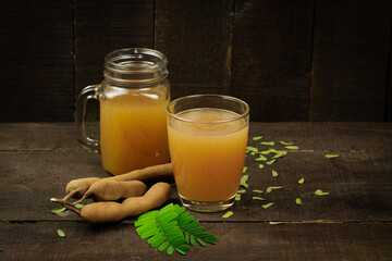 Tamarind juice in glass and tamarind fresh tropical fruit with leaf on wooden background.