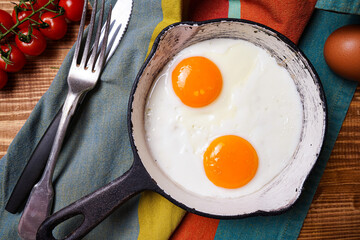 Homemade fried egg in a vintage pan and stylish cutlery on a dark background. View from above.    
