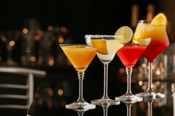 Different delicious cocktails on black table in bar. Space for text