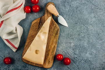 Piece of cow's milk Maasdam cheese on wooden cutting board over concrete bsckground.