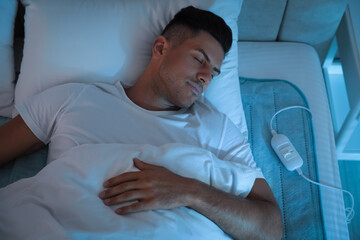 Fototapeta premium Man sleeping on electric heating pad in bed at night, above view
