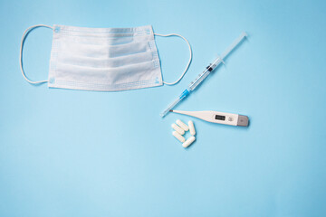 On a blue background are pills, a medical mask, a thermometer and a syringe