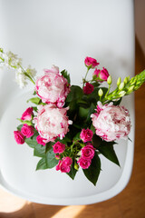 A beautiful bouquet of tender pink peonies and small roses stands on a white chair. Suitable for bridal bouquet, birthday. Close-up, top view.