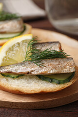 Delicious sandwich with sprats, cucumbers, lemon and dill on wooden board, closeup