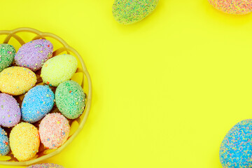 Multi-colored Easter eggs in a basket on a yellow background Spring decor. Copy space text