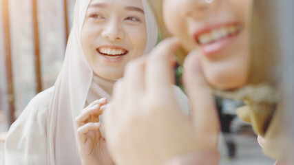 Young beautiful Asian Muslim women enjoying a relaxing moment working and playing with mobile phone in the coffee shop on a bright sunny day