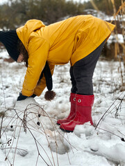 Little girl in yellow jacket and red boots playing in the snow