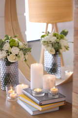 Beautiful burning candles, books and flowers on table at home