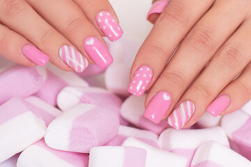 Female hands with pink manicure nails, hearts design on marshmallow background