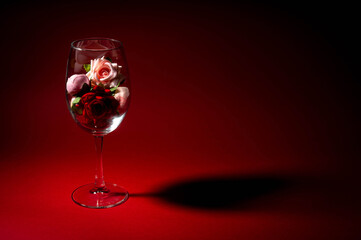 Naklejka na ściany i meble Flowers lie in wine glasses on a red background. Roses and peonies in a glass. The shadow from the glasses on the red surface. Free space. Romance. Festive decoration.
