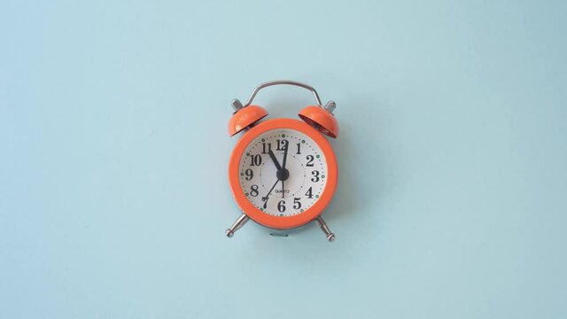Timelapse video of orange alarm clock on blue background at 11:00 am.