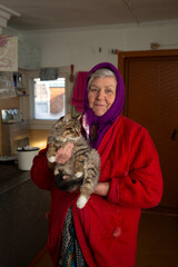 Russian grandmother holds a kitten in her arms, village, Siberia, winter