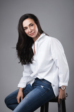 Beautiful middle aged fashion model wearing white shirt and jeans in a photo studio