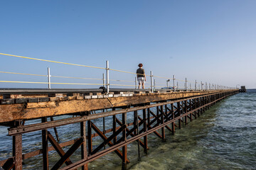 Fototapeta premium a woman walks along a long bridge over a coral reef into the sea