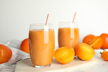 Tasty persimmon smoothie with straws and fresh fruits on white marble table