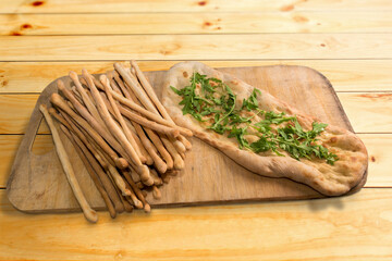 bread sticks and crushed focaccia with oil with rocket leaves on wooden cutting board