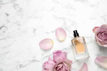 Flat lay composition with bottle of perfume and roses on white marble background, space for text
