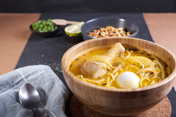 Typical Peruvian dish known as chicken soup, in a wooden bowl with lemon and chives.