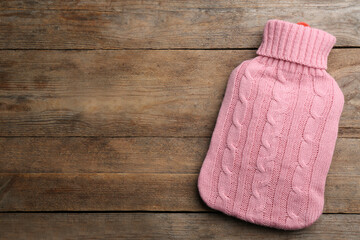 Obraz na płótnie Canvas Hot water bottle with knitted cover on wooden background, top view. Space for text