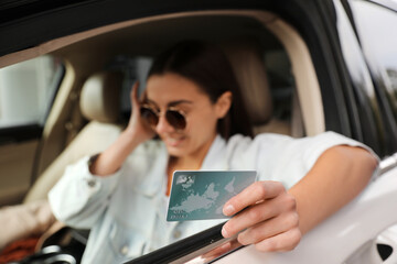 Woman sitting in car and showing credit card at gas station, focus on hand