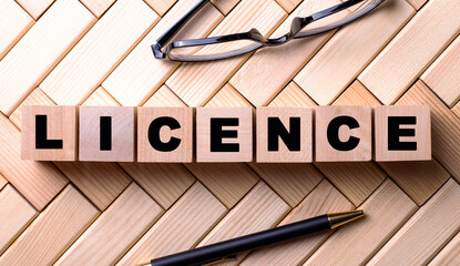 The word LICENCE is written on wooden cubes on a wooden background next to a pen and glasses.