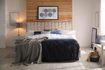 Comfortable bed with pillows and soft blanket in room. Stylish interior design