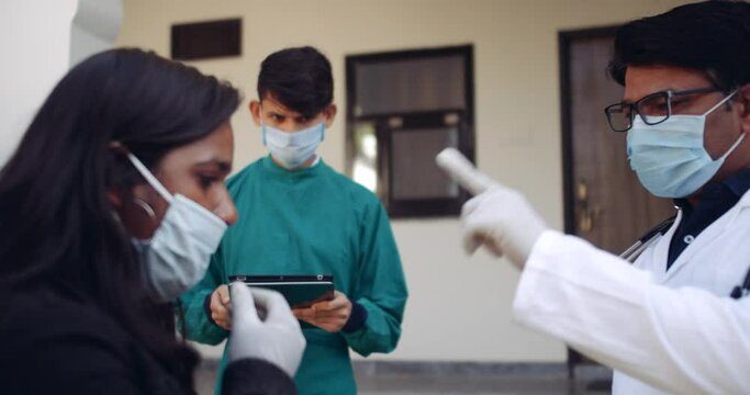 Hospital Medical Staff Men Scan A Young Adult Woman Maintaining Social Distance With Infrared Thermometer Taking Notes Input Data Using Laptop Tablet Computer Technology Digital Device At Entry 