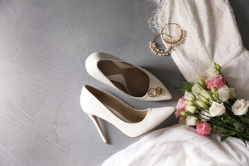 Flat lay composition with wedding dress, white high heel shoes and flowers on grey background. Space for text