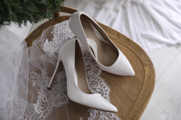 Pair of white high heel shoes, veil and wreath on wooden chair indoors, above view. Dressing for...
