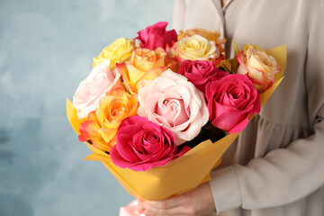 Woman holding luxury bouquet of fresh roses on light blue background, closeup