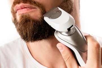Handsome bearded man is using electric trimmer