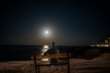 Fototapeta na wymiar woman sits on a bench and looks at the rising moon over the sea at night