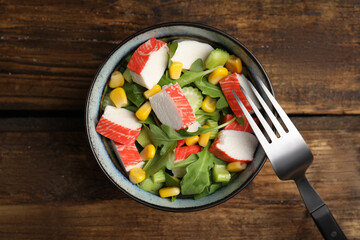 Tasty crab stick salad and fork on wooden table, top view