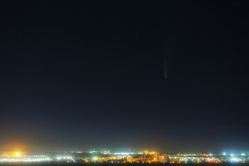 Bright comet C / 2020 F3 (NEOWISE) in the starry night sky. Deep space object over a city with bright street lighting.