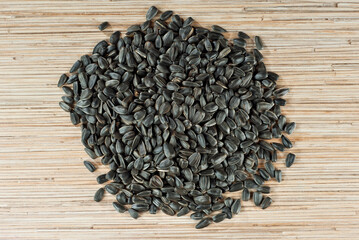 Black sunflower seeds on a yellow board. Texture of nuts on a wooden bamboo table. Lots of nuts in a pile. .