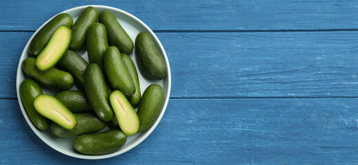 Fresh seedless avocados in ceramic bowl on blue wooden table, top view. Space for text
