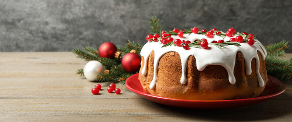 Traditional Christmas cake decorated with glaze, pomegranate seeds, cranberries and rosemary on wooden table, space for text. Banner design