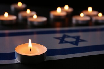 Burning candle and flag of Israel on black table. Holocaust memory day - obrazy, fototapety, plakaty