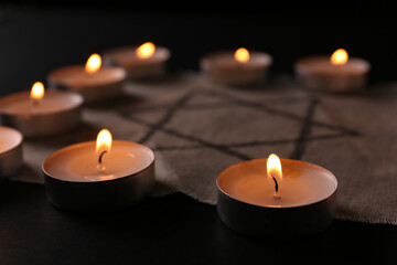 Fabric with star of David and burning candles on black background, closeup. Holocaust memory day