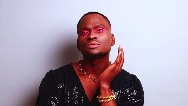 afro american man in dress style with pink eyeshadow and lipstick crossdressing in fashion show studio background
